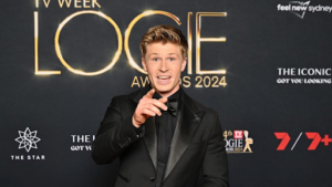 Television presenter Robert Irwin smiling broadly while wearing a sleek tuxedo on a glamorous red carpet.