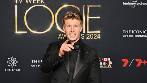 Television presenter Robert Irwin smiling broadly while wearing a sleek tuxedo on a glamorous red carpet.