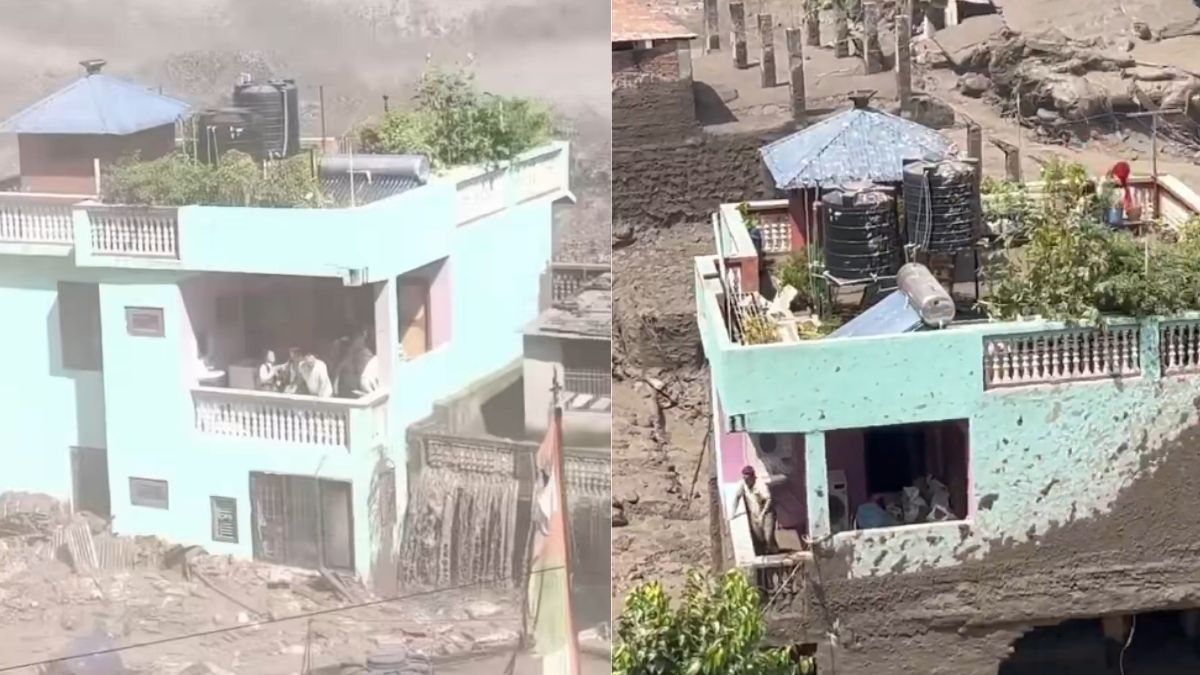 A mint-green house standing intact in Nepal surrounded by raging brown floodwaters and river debris.
